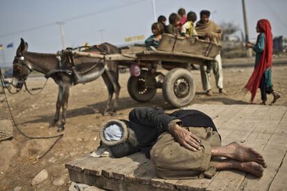 Un grupo de ni&ntilde;os afganos juega en las afueras de Islamabad sobre un carro cuyo due&ntilde;o descansa tumbado en el suelo.