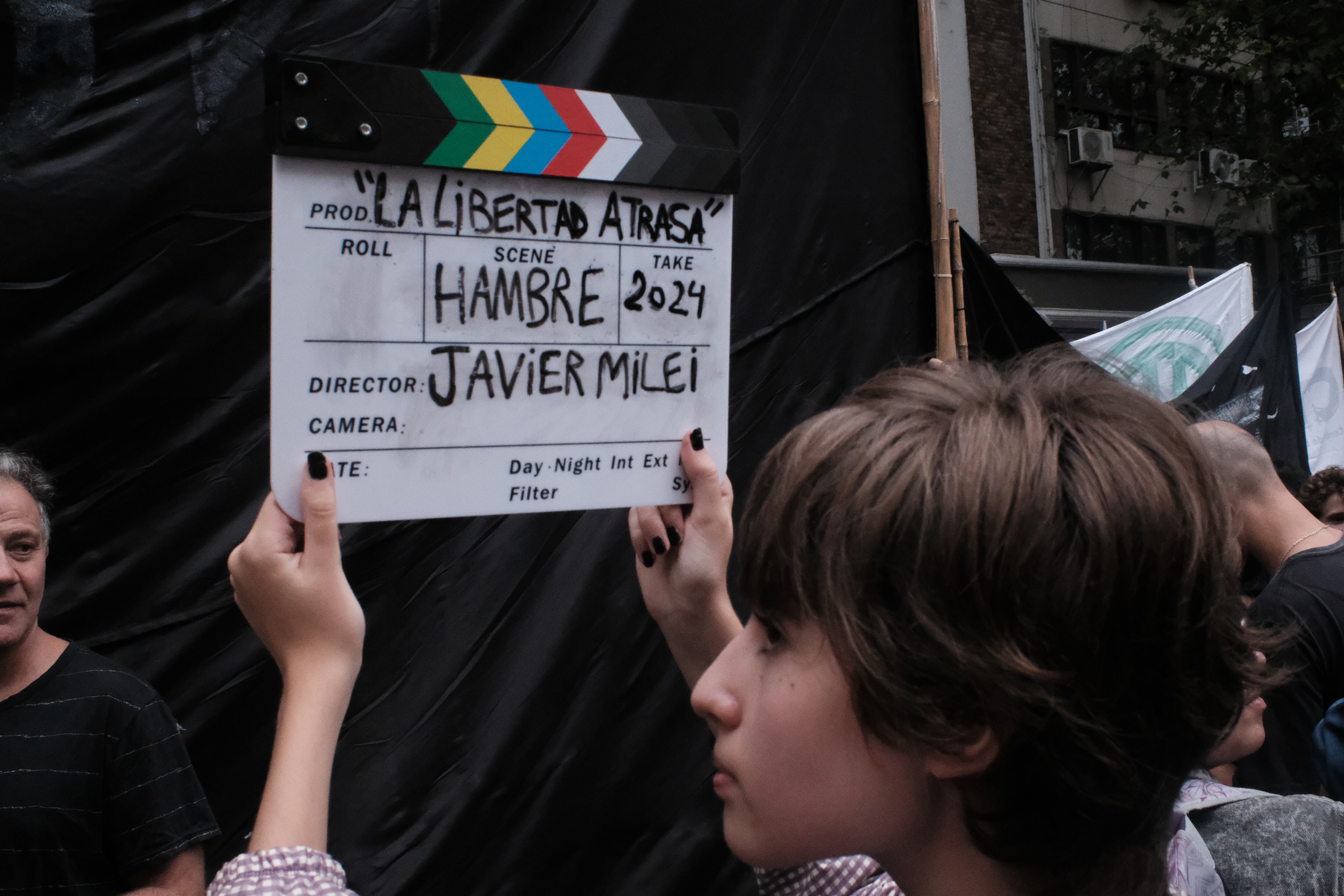 Un joven sostiene una claqueta con un mensaje en contra del presidente Javier Milei.