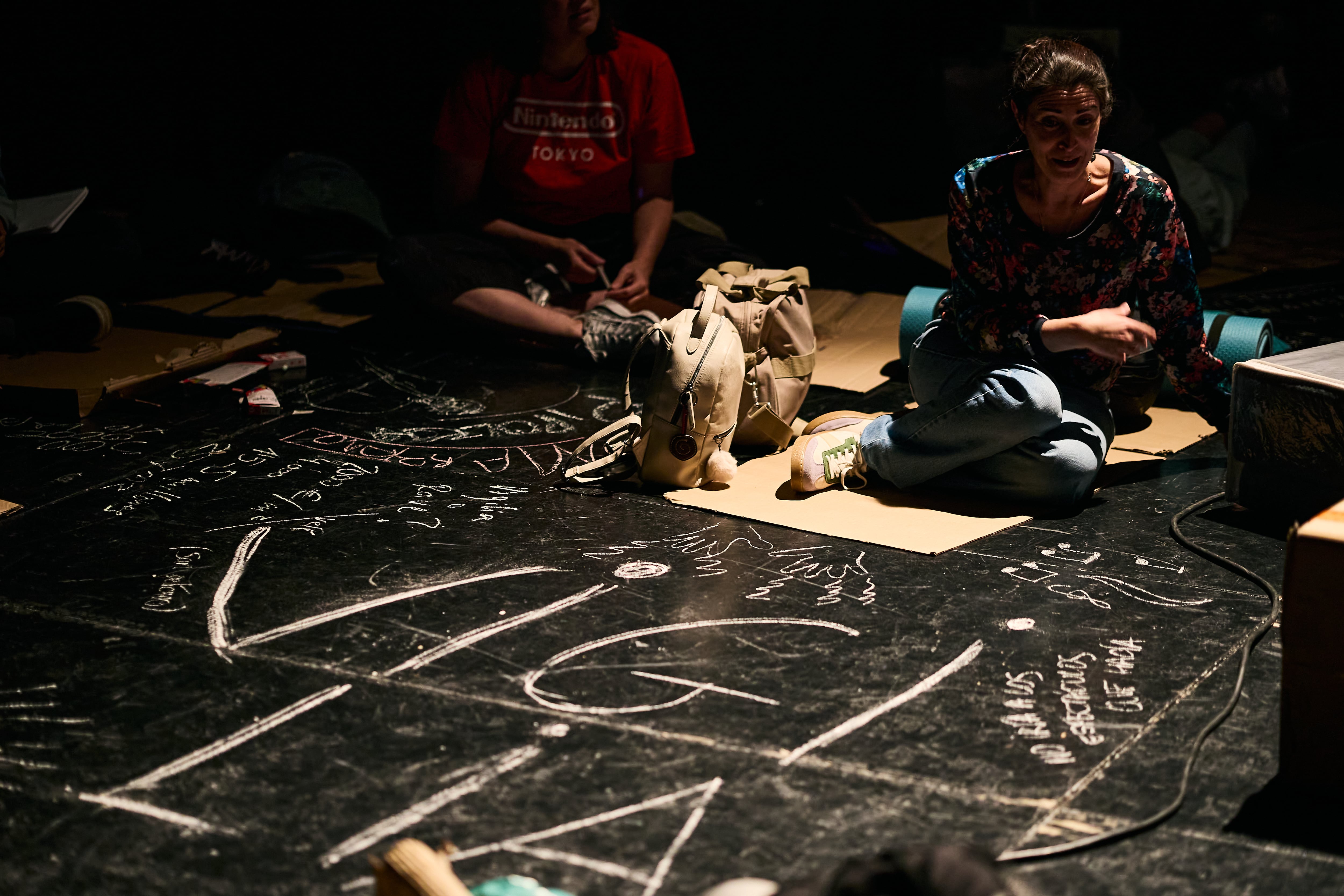 Los participantes escriben con tiza sobre el suelo negro conceptos ligados a la vigilia, durante las 24 horas de encierro en Sevilla.