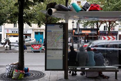 Migrantes esperan bajo la parada de autobús durante la evacuación del campamento improvisado en París.