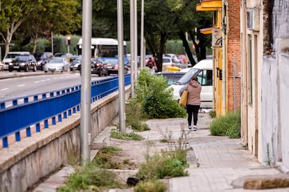 Una mujer camina por la acera en mal estado de la avenida de los Poblados de Madrid, junto a una autovía urbana.