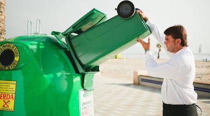 Un camarero vierte un cubo de envases de vidrio en un contenedor de Ecovidrio.