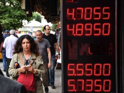 Unos ciudadanos turcos pasan por delante de una pantalla que indica el cambio de dólares a liras, en Estambul.