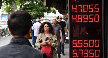 Unos ciudadanos turcos pasan por delante de una pantalla que indica el cambio de dólares a liras, en Estambul.