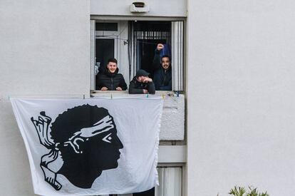 Activistas nacionalistas se asoman por una ventana de la que cuelga una bandera nacional durante la visita del presidente franc&eacute;s, Emmanuel Macron, a Bastia, en la isla de C&oacute;rcega.  