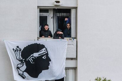 Activistas nacionalistas se asoman por una ventana de la que cuelga una bandera nacional durante la visita del presidente francés, Emmanuel Macron, a Bastia, en la isla de Córcega.