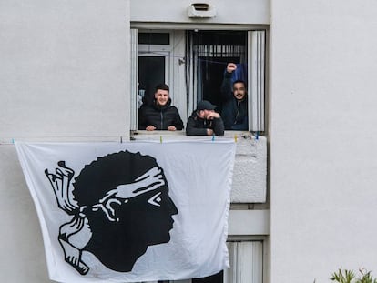 Activistas nacionalistas se asoman por una ventana de la que cuelga una bandera nacional durante la visita del presidente franc&eacute;s, Emmanuel Macron, a Bastia, en la isla de C&oacute;rcega.  