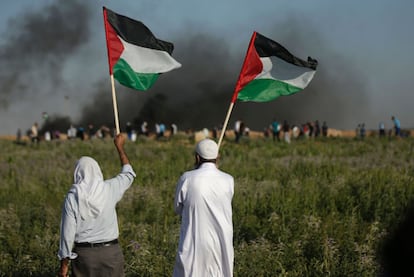 Manifestantes palestinos ondean banderas nacionales mientras miran como sus compañeros se enfrentan a las fuerzas de seguridad israelíes cerca del campamento de refugiados de Jabalia, en la Franja de Gaza.
