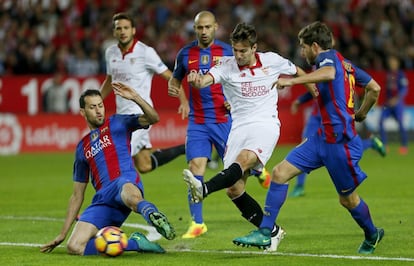 El delantero argentino del Sevilla, Luciano Vietto (2d), golpea el balón ante los jugadores del F. C. Barcelona, el centrocampista Sergio Busquets (i) y el defensa Sergi Roberto