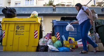 Una mujer deposita una bolsa de basuras en contenedores llenos de C&aacute;diz.