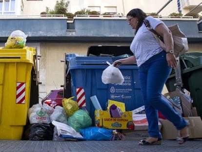 Una mujer deposita una bolsa de basuras en contenedores llenos de Cádiz.