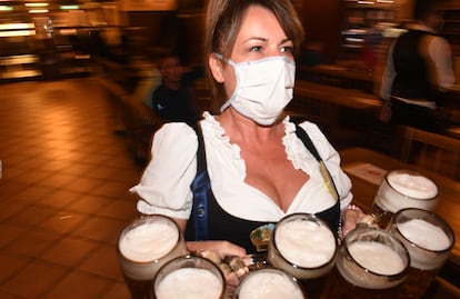 Una camarera sirve cervezas en un local alemán cerrado protegida con una mascarilla.