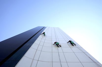 Tres trabajadores limpian las ventanas y la fachada de un edificio de oficinas en Baku, Azerbaiyán.