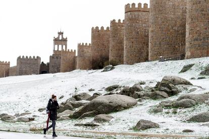 Una mujer camina junto a la muralla de Ávila cubierta por una fina capa de nieve caída en las últimas horas. La llegada de una borrasca a la península trae consigo en los dos próximos días un tiempo con copiosas nevadas, especialmente en la cordillera cantábrica, además de lluvias, viento, olas de diez metros en el litoral noroeste y temperaturas de hasta ocho grados menos.