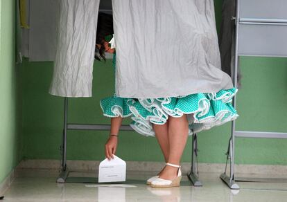 Una joven vestida de flamenca recoge del suelo su voto en una cabina del colegio electoral de la Fuensanta de Córdoba, donde las elecciones municipales coinciden con la celebración de la Feria de esta ciudad.