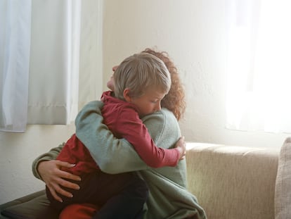 Una madre abraza a su hijo en el salón de su casa.