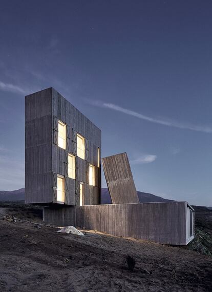<p>Vista exterior y nocturna del edificio. En el bloque iluminado se encuentran las habitaciones.</p><br> <p> Ni oculta ni envuelta por el paisaje, esta casa que Alejandro Aravena firmó con su estudio Elemental no se esconde en el paraje: se clava en él. Como un monumento megalítico, se asoma a un acantilado de la costa de Los Vilos, en la región de Coquimbo, al norte de Santiago de Chile, para mirar al océano Pacífico. Tres volúmenes de hormigón —uno horizontal, uno vertical y uno oblicuo— forman una vivienda escultórica que está pensada con gran funcionalidad. Se puede abrir y usar por partes. La base contiene la cocina, el salón, el dormitorio y el baño principal. En el prisma vertical se encuentran los tres dormitorios. El inclinado es el tiro de la chimenea que, reforzando el carácter primitivo, Aravena define como una hoguera. El amueblamiento es sobrio pero escogido, blanco sobre el fondo gris del hormigón. La madera utilizada en la azotea y en la cocina es la que se empleó para los encofrados de los muros. Los peldaños de la escalera o la estructura de la mesa contrastan con las paredes desnudas en esta sorprendente vivienda. </p>