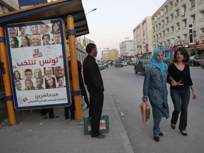 Dos jóvenes pasean junto a un cartel que reza "Túnez vota".