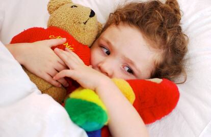 Niña pequeña en su cama abrazada a sus peluches