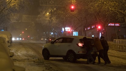Varias personas empujan un coche atascado por la nieve en Madrid.