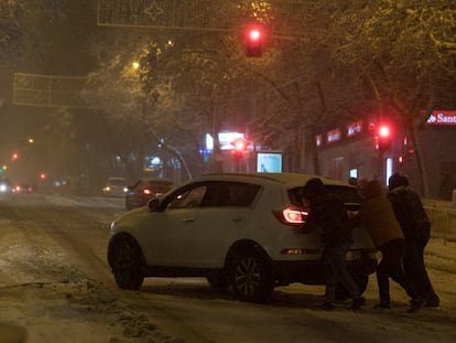 Varias personas empujan un coche atascado por la nieve en Madrid.