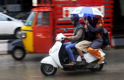 Un conductor lleva a su hija y a su mujer, que sostiene un paraguas, durante las fuertes lluvias en Bangalore (India).