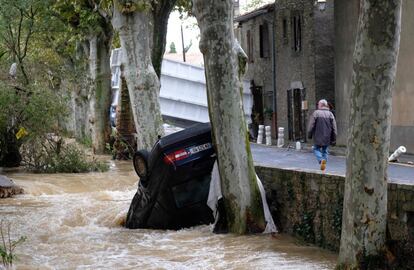 Un residente camina junto un coche atrapado en un rio, en  Villegailhenc, al sur de Francia.