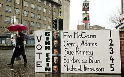 Una mujer pasa junto a un cartel que pide el voto para la candidatura del Sinn Fein en Belfast.