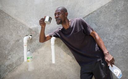 Frantz Terin llena un cazo de agua en la fuente junto a su negocio.