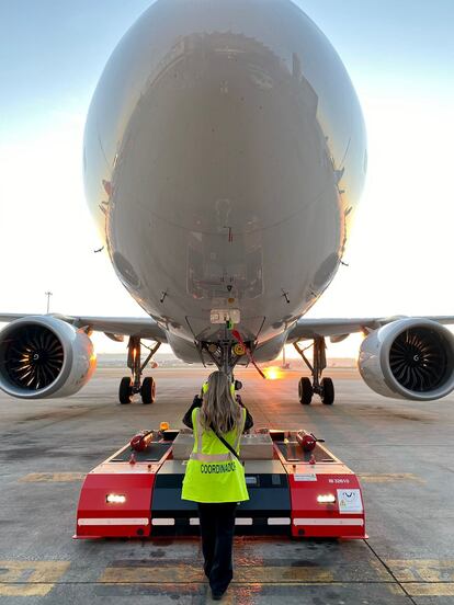 Una operaria de Iberia dirige el movimiento de un avión a través de un remolcador o tractor de pushback.