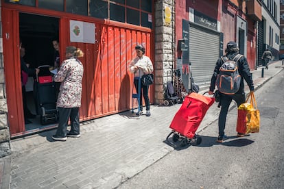 Varias personas beneficiarias de la ayuda de la asociación esperan su turno frente a la sede de  la Asociación Farmacéuticos Solidarios, en Vallecas, Madrid.