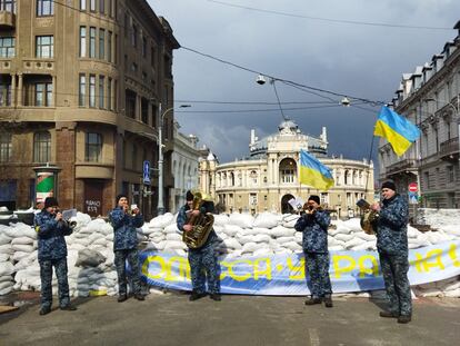 A group of musicians plays in front of a barricade in Odessa in March 2022, with the Opera building in the background.