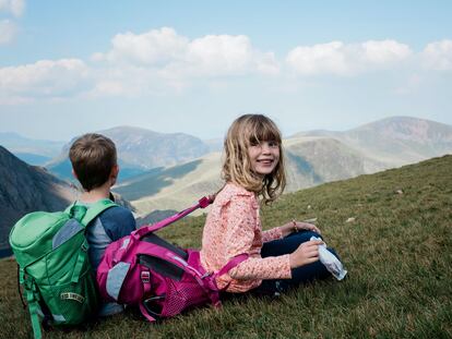 Una niña y un niño llegan a la cima de una montaña en un viaje de senderismo, en una foto de archivo.
