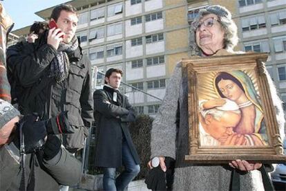 Una mujer con un cuadro del Papa espera noticias a las puertas del hospital junto a decenas de periodistas.