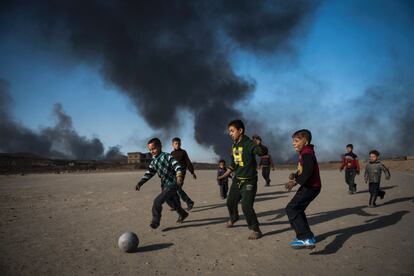 Un grupo de niños juegan al fútbol con columnas de humo de pozos petrolíferos incendiados, provocados por el Estado Islámico, en la ciudad de Qayyarah, a unos 70 kilómetros al sur de Mosul el 20 de noviembre.