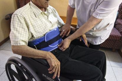 Una auxiliar geriátrica coloca una contención física de cintura.