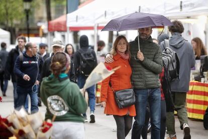 Una pareja camina entre los puestos de libros y rosas en La Rambla.