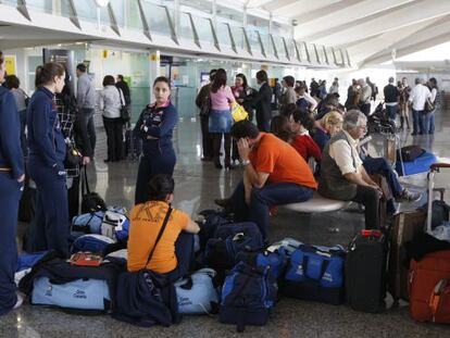 Varios viajeros esperan ante un mostrado del Aeropuerto de Loiu en una imagen de archivo.