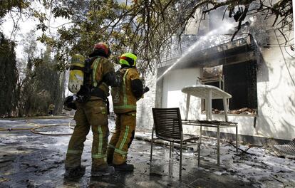 Dos bomberos refrescan el interior de una de las viviendas afectadas por el incendio forestal de Llutxent , el 8 de agosto.