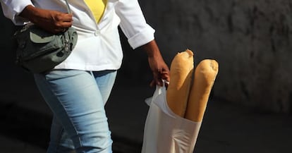 Una mujer camina con dos barras de pan en una bolsa de pl&aacute;stico.