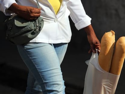 Una mujer camina con dos barras de pan en una bolsa de pl&aacute;stico.