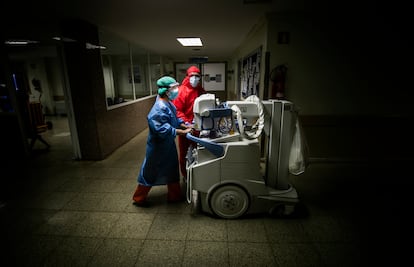 Dos trabajadores del hospital trasladan una unidad móvil de radiodiagnóstico por un pasillo del hospital. 