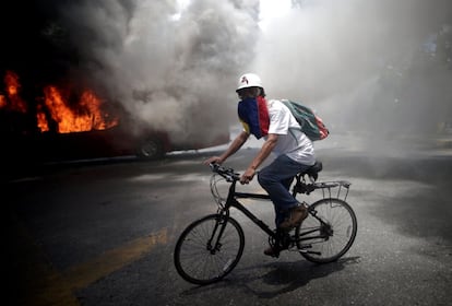 Un manifestante de la oposición monta una bicicleta frente a un autobús en llamas cerca de la base aérea de La Carlota en Caracas.