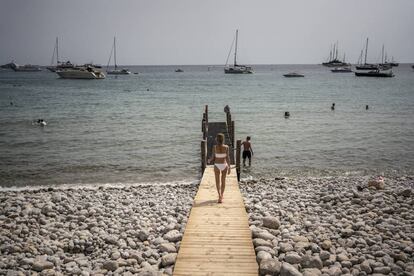 Varias personas se bañan, con los barcos fondeados de fondo, en la cala Jondal de Ibiza.