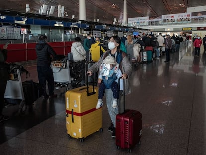 Una mujer lleva a su bebé mientras empuja dos maletas en el aeropuerto de Pekín.