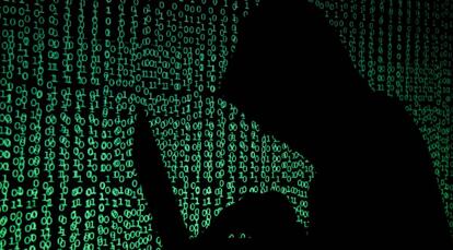 Un hombre encapuchado sostiene un portátil mientras se proyecta un código cibernético tras él.