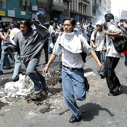 Los manifestantes corren mientras la policía <b>antidisturbios</b> arroja gases lacrimógenos frente al palacio presidencial en Quito.