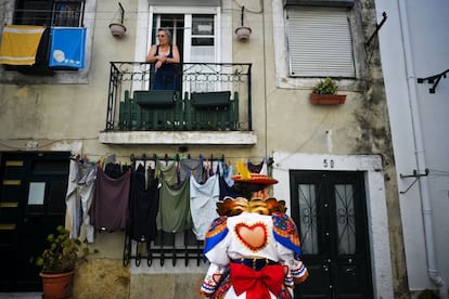 Una mujer observa desde su balcón en el barrio tradicional de Alfama cómo una mujer con traje tradicional camina antes de participar en el desfile.