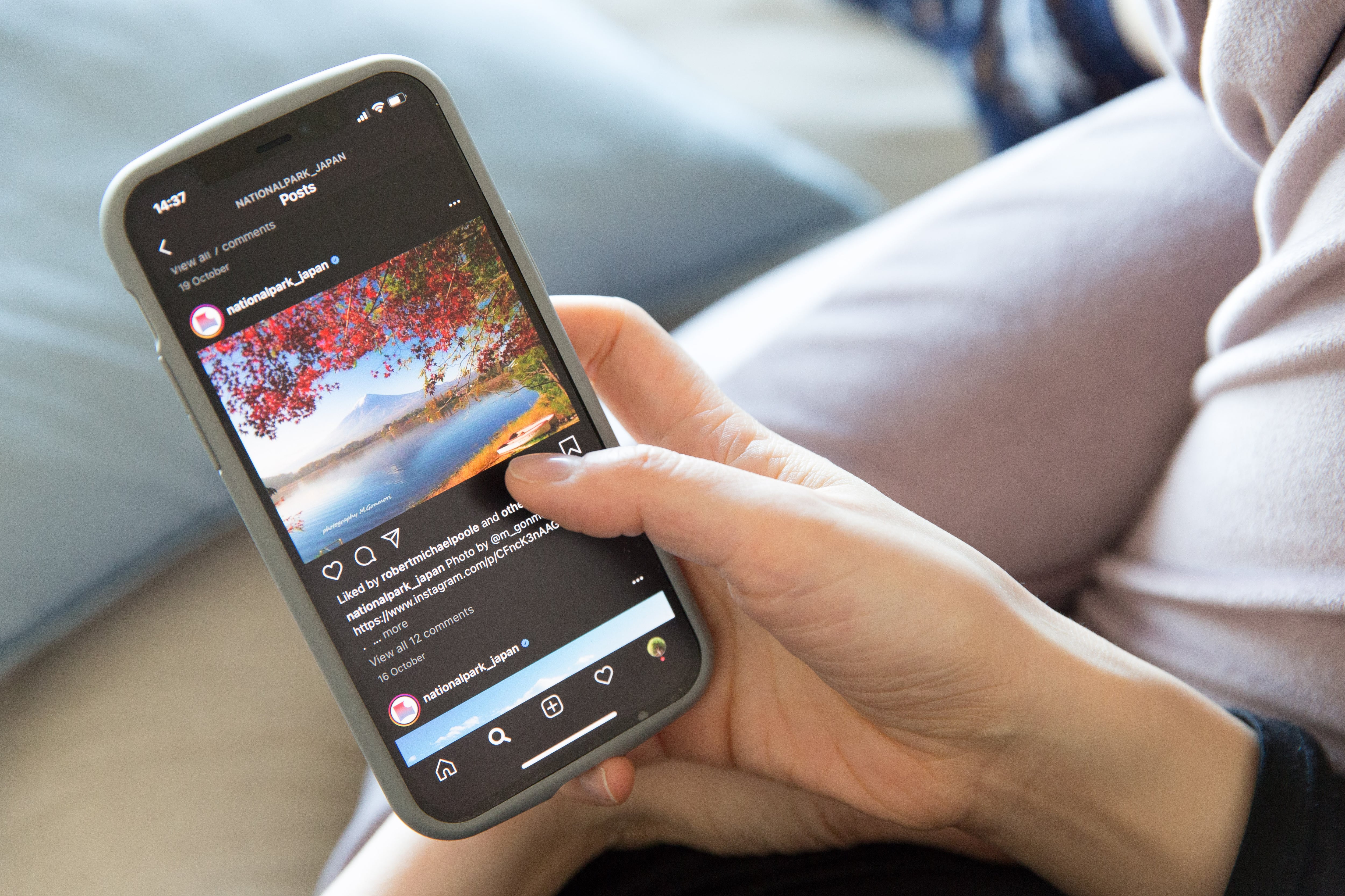 Una mujer sostiene un iPhone 12 mientras revisa el feed de Instagram.
