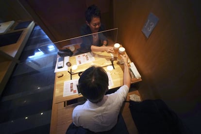 Dos clientes hacen un brindis separados por un plástico en un restaurante de Tokio (Japón).